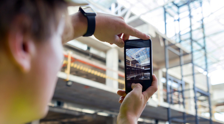 Persona tomando una foto con un teléfono móvil dentro de un edificio en construcción con estructuras de acero y concreto visibles.